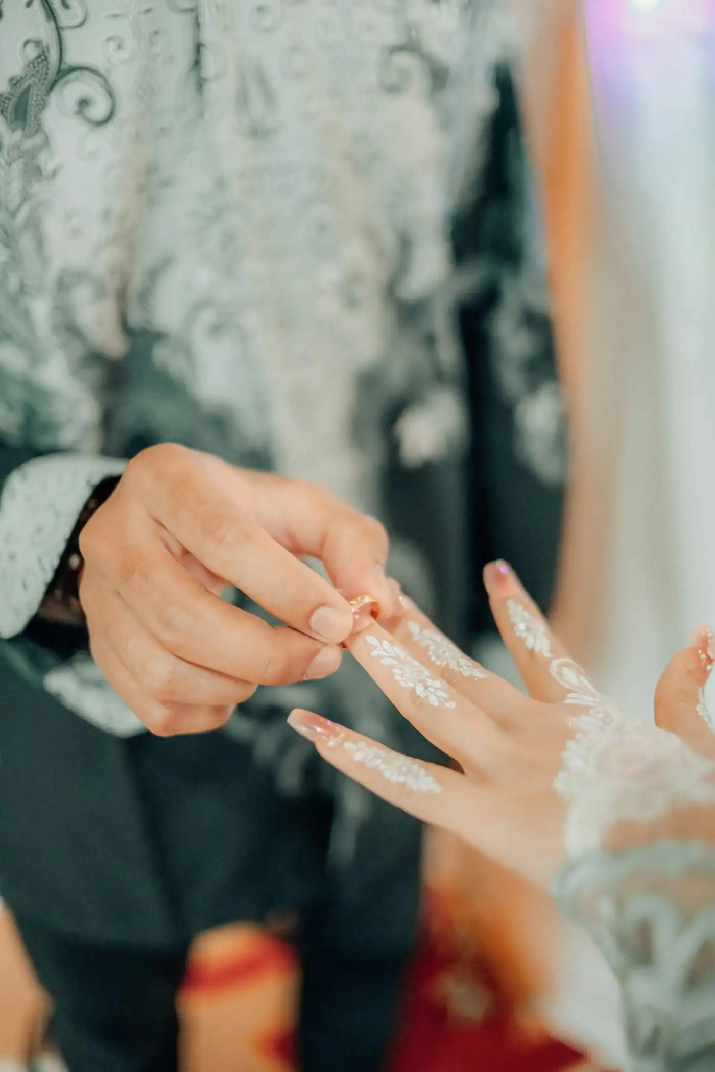 The groom sliding a ring onto the bride’s henna-decorated finger