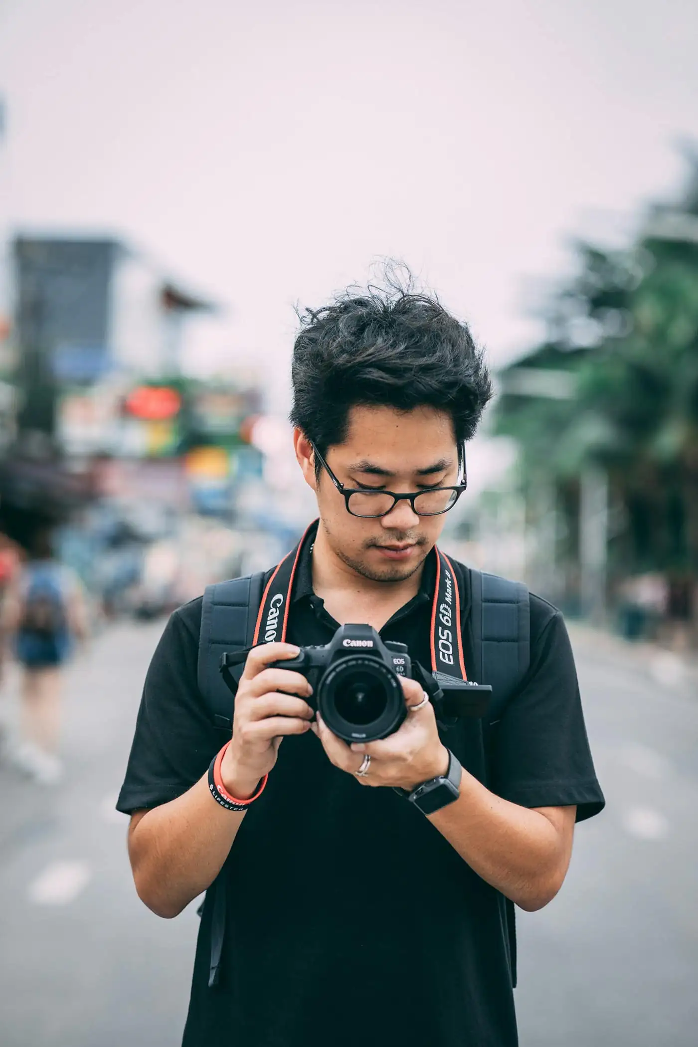 Adli Rahman, lead photographer, looking down at the camera in his hands on a busy street